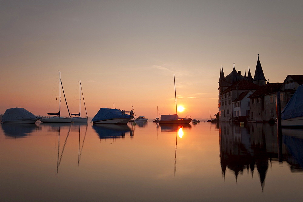 Turmhof building in Steckborn on Lake Constance at sunrise with boats on buoys and reflections in the water, Switzerland, Europe