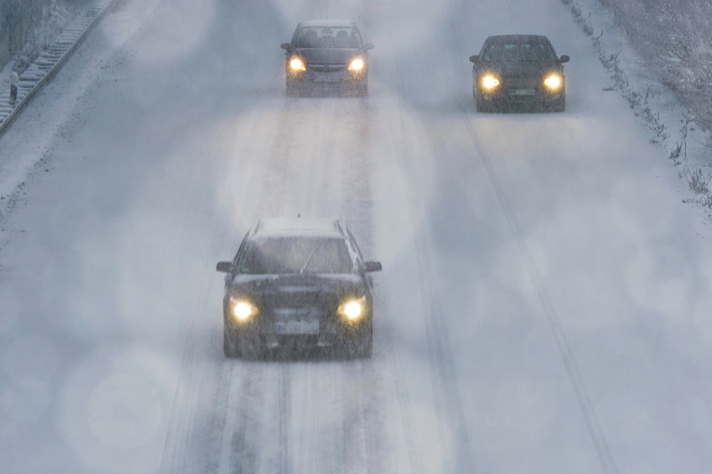 Three cars driving in a snow flulrry on a highway