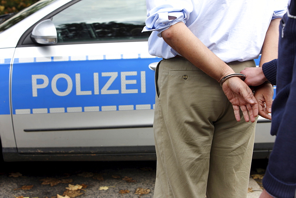 Man in a suit is led off in handcuffs by a police officer