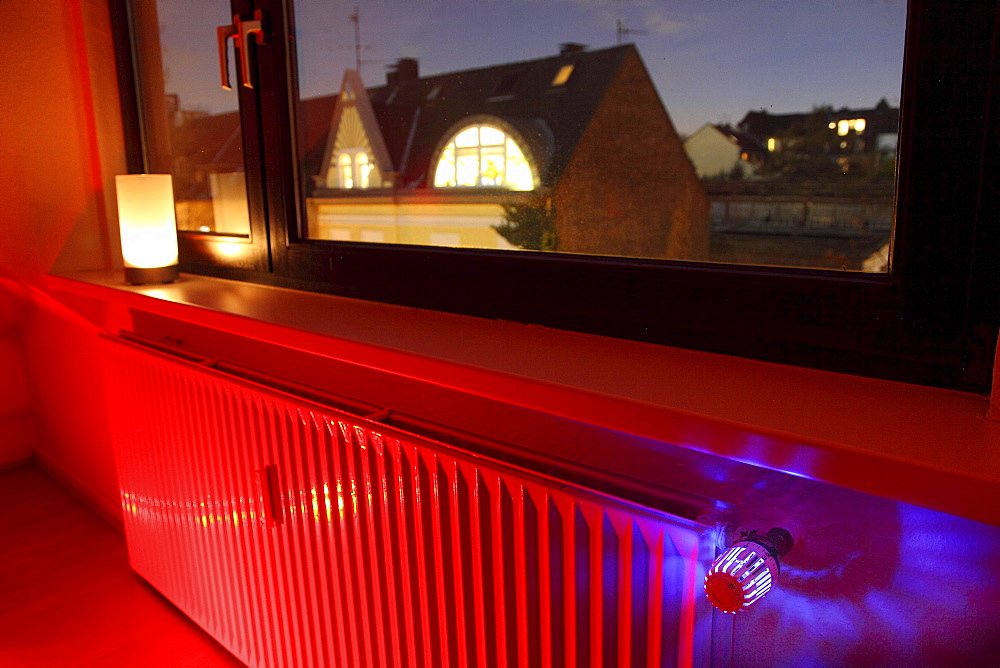 Radiator at a window with an illuminated thermostat, heating costs