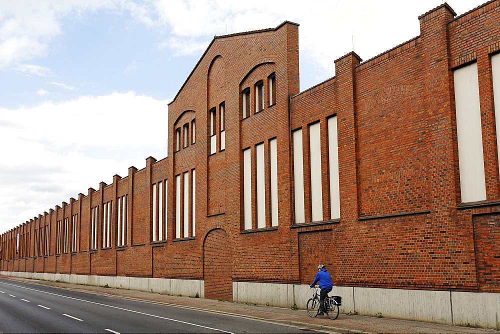 Cyclist riding past the brick facade of a former factory, Batteriestrasse, industrial port of Neuss, Niederrhein, North Rhine-Westphalia, Germany, Europe