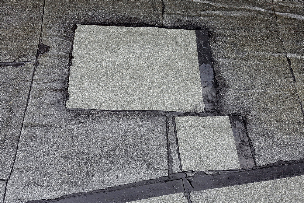 Patched-up, repaired areas on a roof made of roofing felt