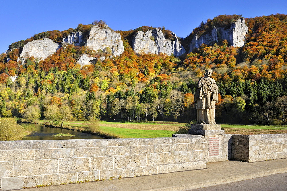 Hausener Bogenbruecke arch bridge with the statue of St. Nepomuk, patron saint of bridges, in front of the peaks of the Hausener Zinnen amidst autumnal vegetation, Sigmaringen district, Baden-Wuerttemberg, Germany, Europe