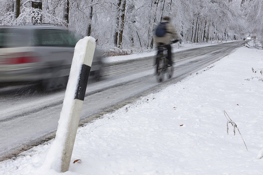 Cyclist being overtaken on a snowy country road in winter, Hesse, Germany, Europe