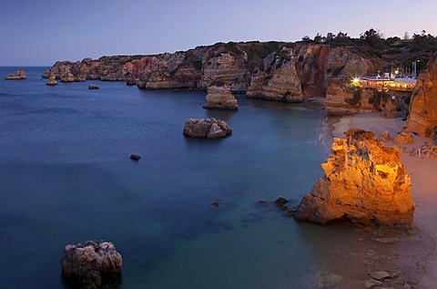 Rugged rocky coastline with illuminated restaurant in the evening light, Lagos, Algarve, Portugal, Europe