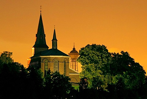 Parish church and water tower with sky lit by Duisburg steel works, Lank-Latum, Meerbusch, North Rhine-Westfalia, Germany, Europe