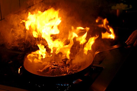 Explosive flame in a frying pan with fried meat on a gas stove with fat which is too hot