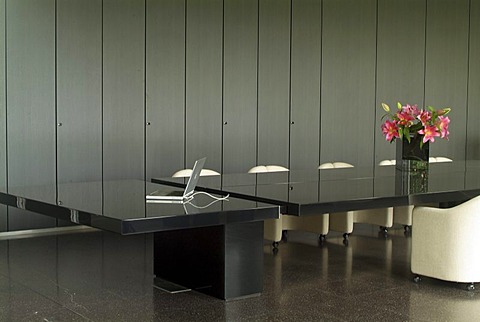 Detailed view of an exclusive black shiny conference table with empty white leather chairs