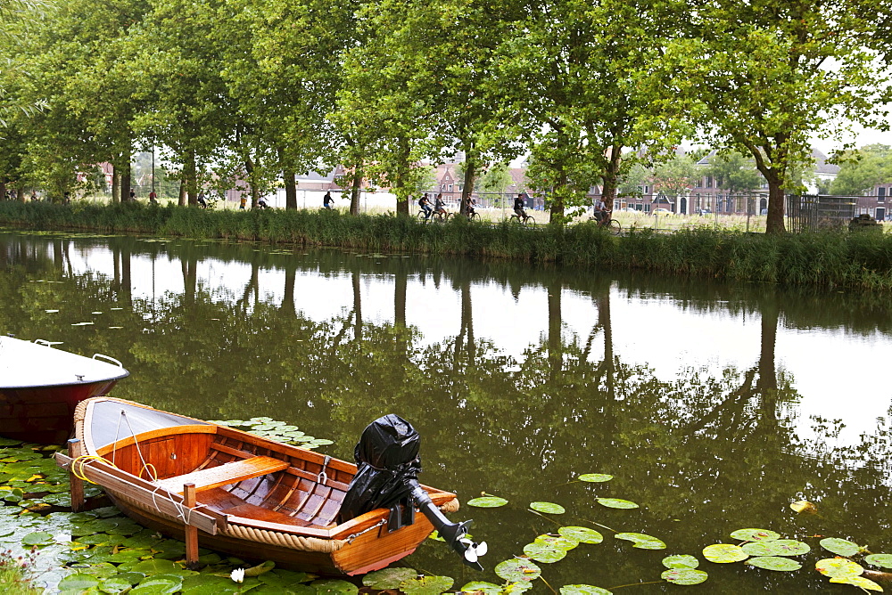 Canal with trees reflected in the water, tourists riding bicycles and small boat, Edam, Holland, Netherlands, Europe