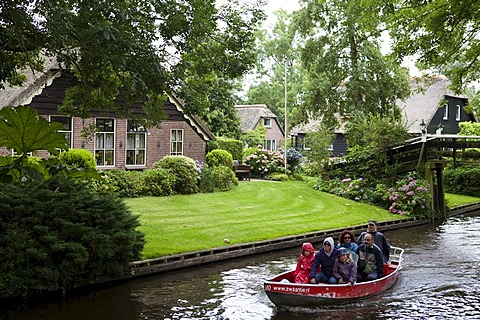 Traditional Dutch housing with garden beside the canal, tourists on a red boat visiting the village, Giethoorn, Flevoland, Netherlands, Europe