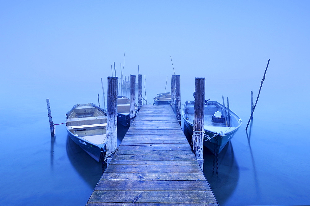 Fishing pier with fishing boats in the morning mist on the shore of Iznang, Landkreis Konstanz county, Baden-Wuerttemberg, Germany, Europe