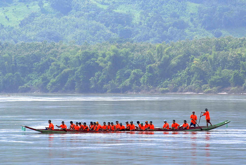 Dragon boat with a great team in orange t-shirts at the dragon boat race on the Nam Ou River, Luang Prabang, Northern Laos, Laos, Southeast Asia