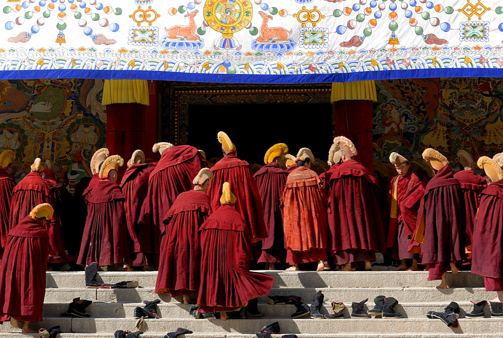 Tibetan monks wearing robes and yellow hats of the Gelug Order or Yellow Hat Sect on the stairs in front of the Assembly Hall, Tibetan Dukhang, the Labrang Monastery, Xiahe, Gansu, China, Asia