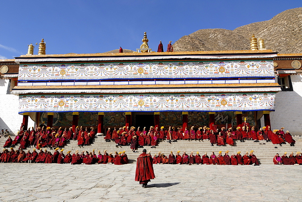 Tibetan monks wearing robes of the Gelug Order sitting on the stairs in front of the Assembly Hall, Tibetan Dukhang, the Labrang Monastery, Xiahe, Gansu, China, Asia