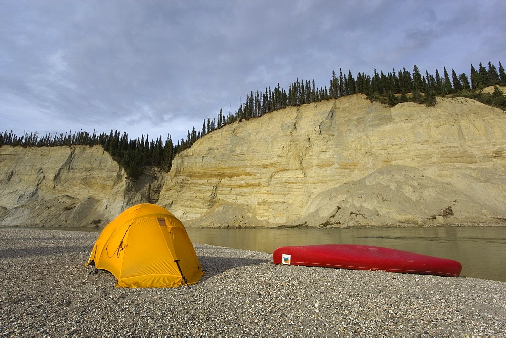 Camp, tent and canoe on a gravel bar, high cut bank, river cliff, erosion, behind, upper Liard River, Yukon Territory, Canada