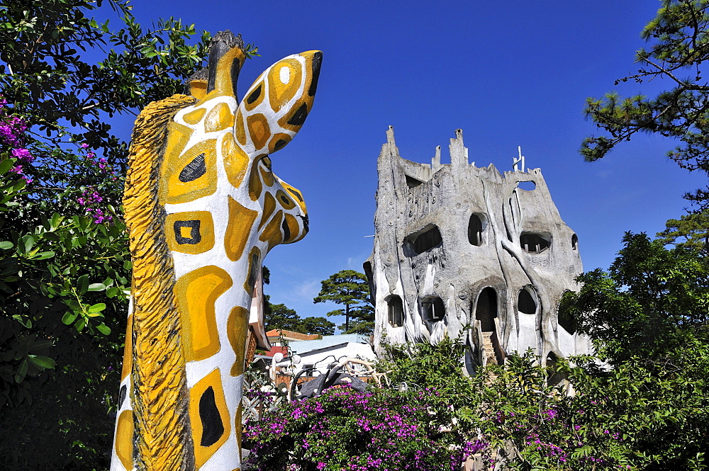 Giraffe statue looking on the bizarre main building of the Crazy House Hotel, Hang Nga Guesthouse, Dalat, Central Highlands, Vietnam, Asia