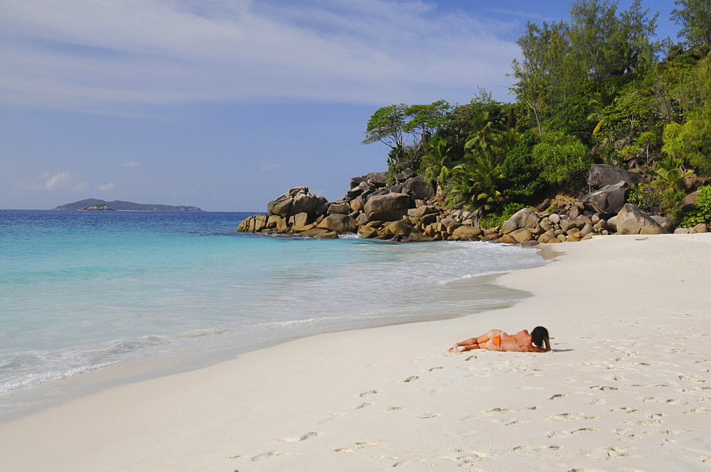 Woman lying on a beach with granite rocks and tropical vegetation, Anse Georgette, Praslin Island, Seychelles, Africa, Indian Ocean