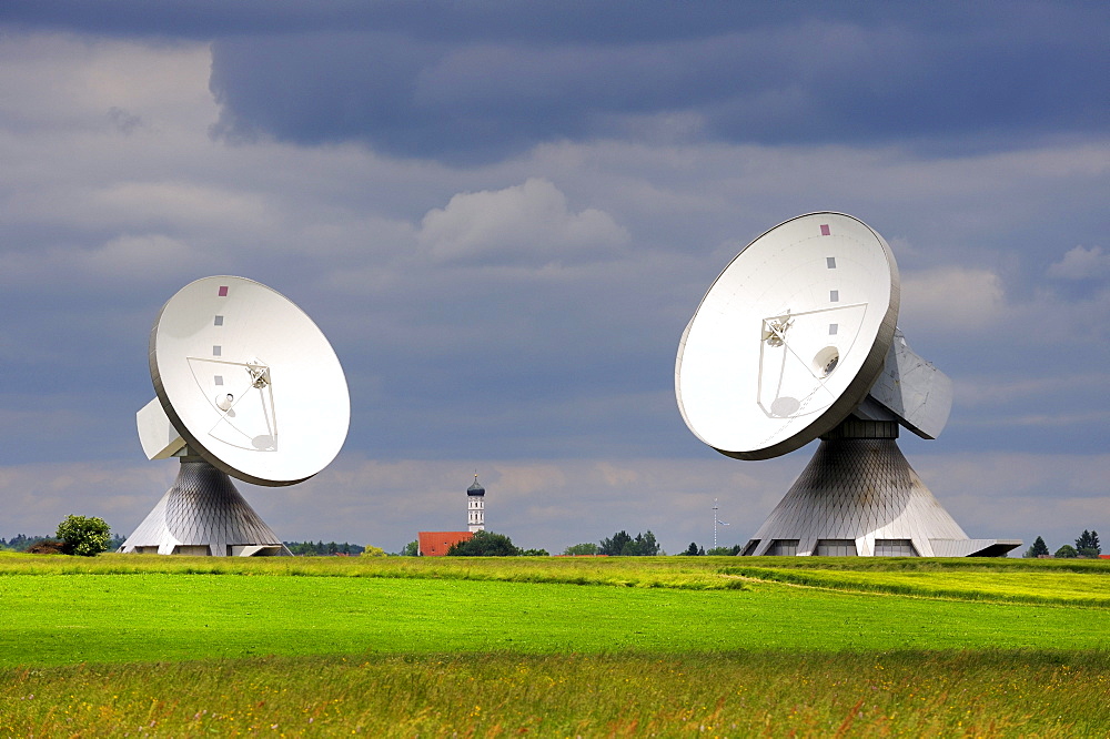 Parabolic antennas at the Erdfunkstelle, station for radio, television and data communications, with the spire of St. Remigius Church in Raisting, district of Weilheim-Schongau, Bavaria, Germany, Europe