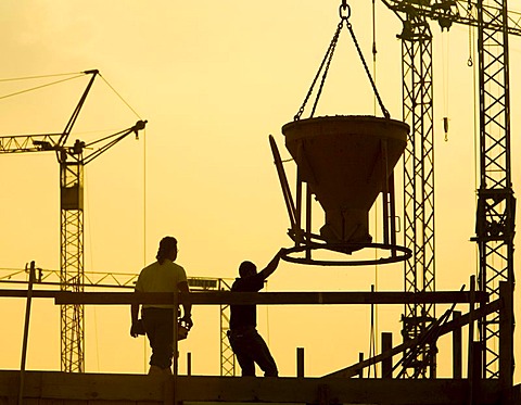 Construction workers working on a building site in front of a backdrop of several cranes in Waltrop, North Rhine-Westphalia, Germany, Europe