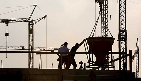 Construction workers working on a building site in front of a backdrop of several cranes in Waltrop, North Rhine-Westphalia, Germany, Europe