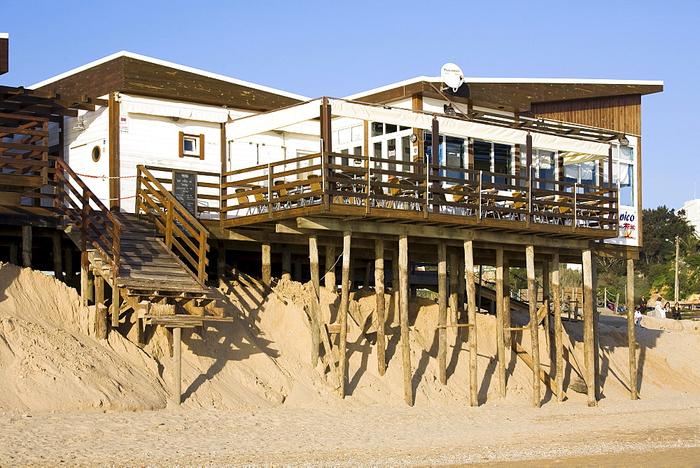 Soil erosion, beach bar on spiles nearly washed away by the sea in the sand by Algarve, Praia Alvor, Portugal, Europe