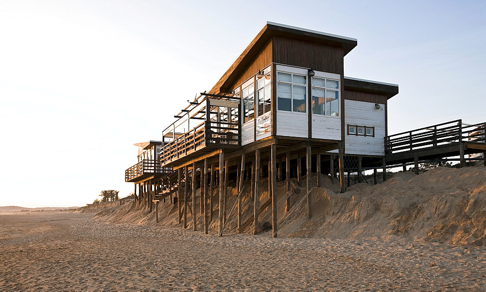 Soil erosion, beach bar on spiles nearly washed away by the sea in the sand by Algarve, Praia Alvor, Portugal, Europe