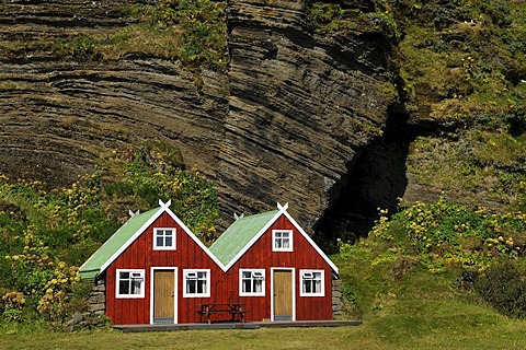 Red holiday homes in front of a rock wall, Vik, South Coast, Iceland, Europe