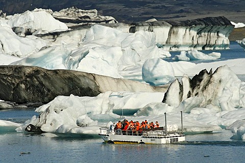 In the Joekulsarlon glacier lagoon of the Vatnajoekull Glacier, people travelling in an boat between the floating icebergs, which are partly coloured by black lava ash, Iceland, Europe