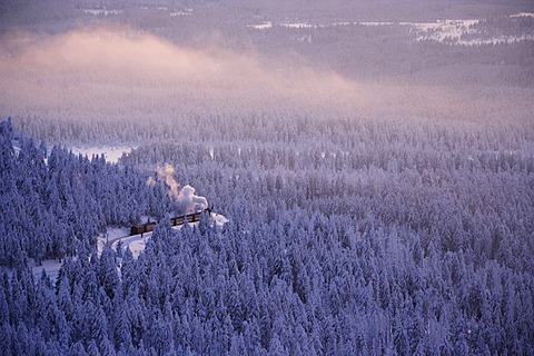 View from the Brocken mountain over a winter landscape deeply covered in snow at sunset and the Harzer Schmalspurbahn, narrow-gauge railway with steam engine, Saxony-Anhalt, Germany