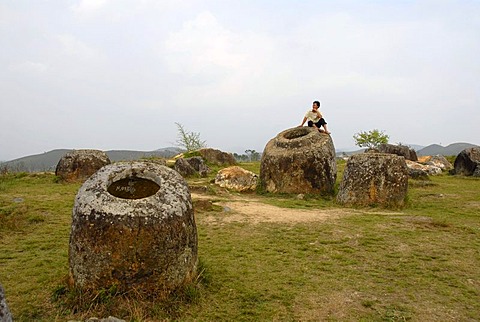 A person sitting on one of the mysterious bellarmines, Plain of Jars, place of discovery No. 1 (Thong Hai Hin), Xieng Khuang Province, Laos, South East Asia