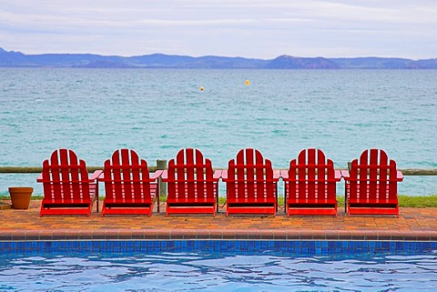 Red deckchairs with view of the ocean, swimming pool in the foreground