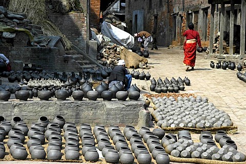 Potter working among many pots put out for drying on Potters' Square Bhaktapur Nepal