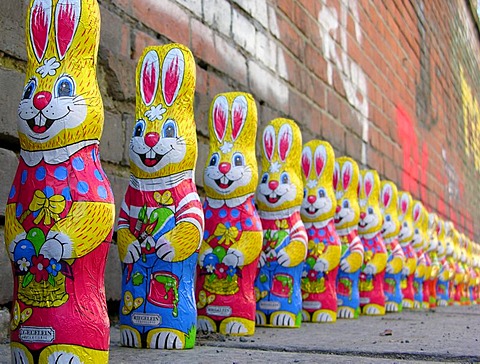 A group of over twenty easter bunnies from chocolate in a row in front of a wall with graffiti