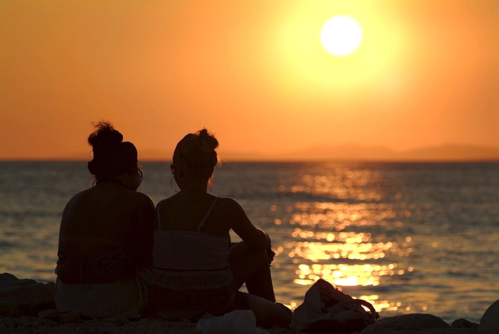 Two women on a beach watching the sunset over the ocean