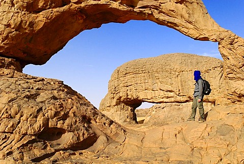 Man standing underneath the rock arch of Youf Ahakit, Tassili du Hoggar, Wilaya Tamanrasset, Algeria, Sahara Desert, North Africa, Africa