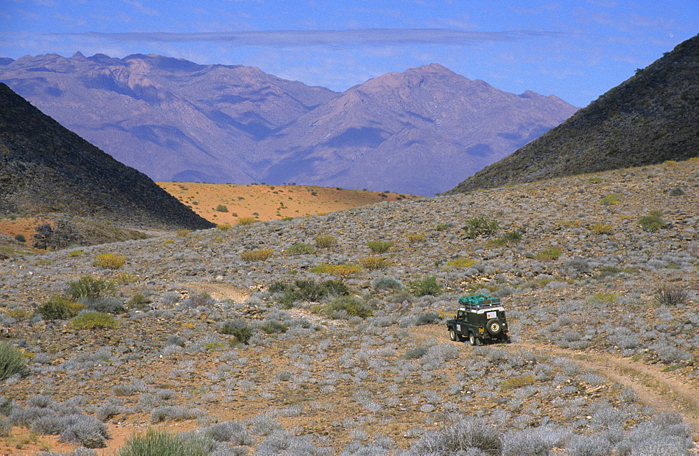 Land Rover in stony desert landscape, Brandberg Mountain backdrop, near Uis, Namibia, Africa