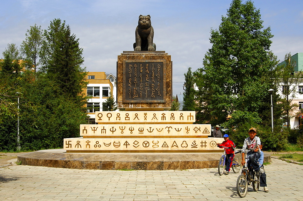 Children cycling past the monument to the Mongolian State Seal, sculpture of a tiger, writing in old Mongolian script, Ulaanbator, Mongolia