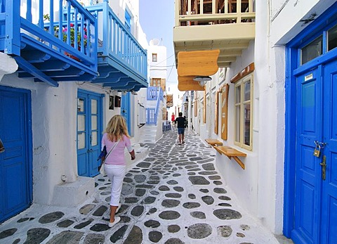 Blonde woman walking through an alleyway sided with blue wooden doors, Mykonos Island, Cyclades, Greece, Europe