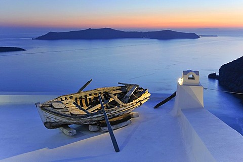 Old rowboat displayed on a rooftop terrace at sunset in front of the blue sea and the volcanic island of Nea Kameni, Thira, Fira, Santorini, Cyclades, Greece, Europe