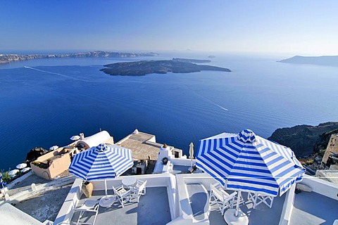 Terraces with blue and white striped sunshades in front of the blue sea and the volcanic island of Nea Kameni, Santorini, Cyclades, Greece, Europe