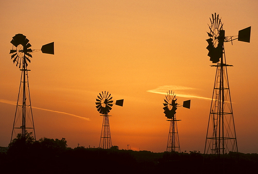 Wind driven water pumps silhouetted against evening sunset sky near Protaras, Cyprus