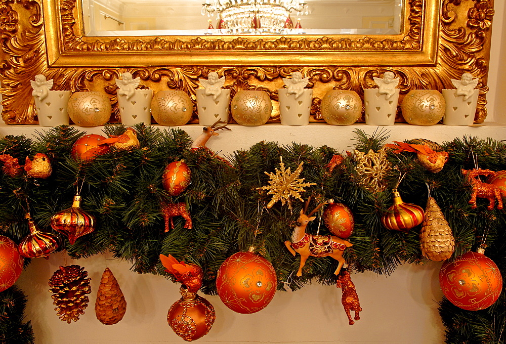 Mantelpiece showing edge of gold-framed mirror, Christmas ornaments hanging from pine sprigs from mantel