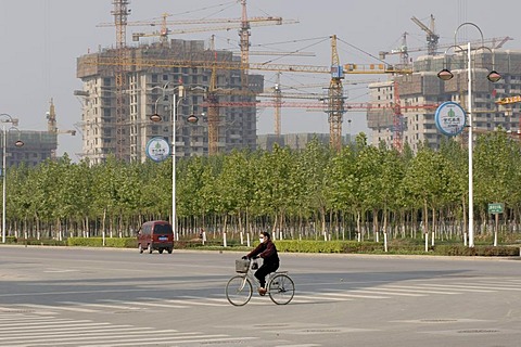 Bicyclist on a street, in the background multi-storey buildings under construction, Beijing, China