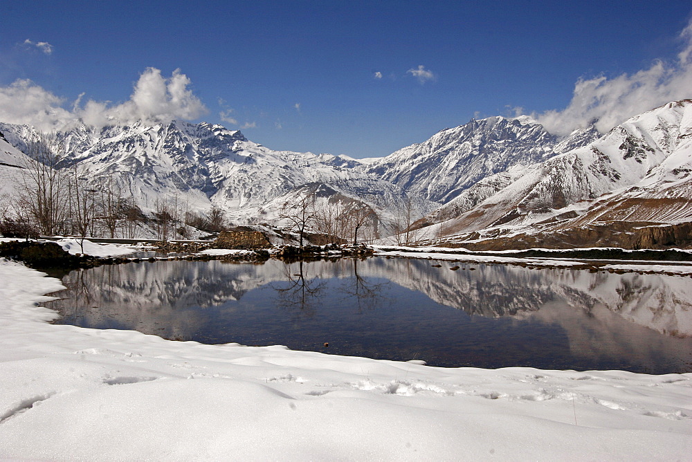 Snow-covered mountains reflected in a lake near the remote mountain village Jharkot along the popular Jomsom Trail, Jharkot, Nepal, Asia