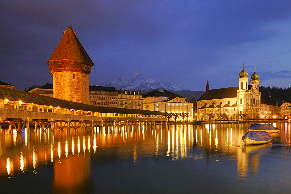 Lights of the Kapellbruecke, Chapel Bridge and St. Francis Xavier Jesuit Church reflected on the surface of the Reuss River, Lucerne, Switzerland