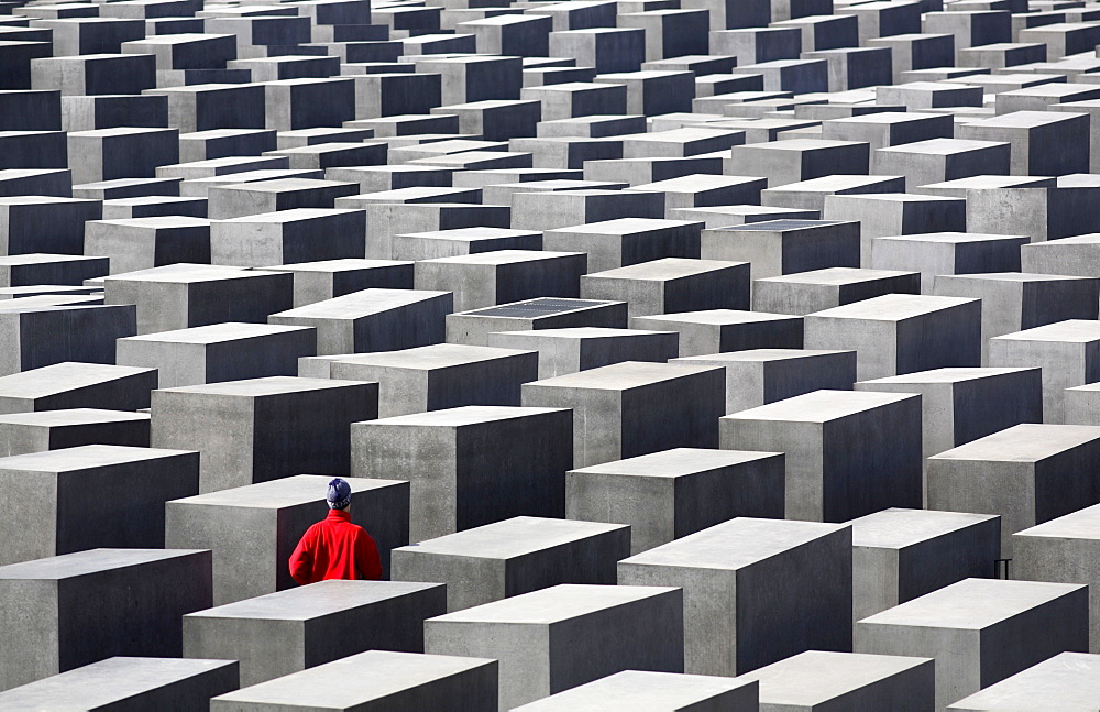 Person in red jacket walking amongst the concrete slabs of the Holocaust Memorial, Berlin, Germany