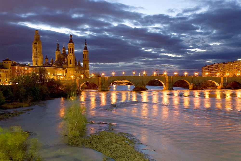 Basilica del Pilar cathedral, Puente de Piedra bridge and the Ebro River lit by street lamps under a twilight sky, dusk in Saragossa or Zaragoza, Aragon, Spain, Europe