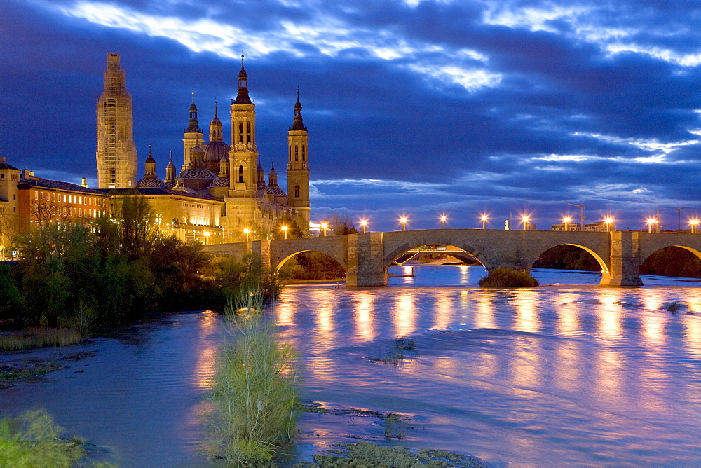 Basilica del Pilar, Basilica of Our Lady of the Pillar beside the Ebro River and the Puente de Piedra Bridge under an evening sky bathed in street lights, Zaragoza (Saragossa), Aragon, Spain