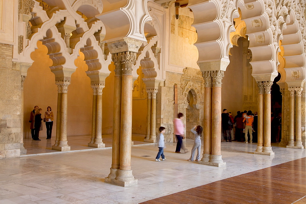 Tourists beneath the ornate stone carved arched passageway of the Santa Isabel Patio, Palacio de Aljaferia palace, Moorish architecture, Zaragoza, Saragossa, Aragon, Spain