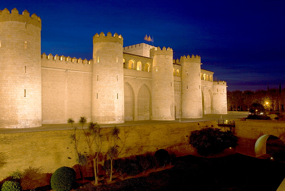 Palacio de Aljaferia palace illuminated at night under floodlights, flags flying over external wall and towers, Moorish architecture, Zaragoza, Saragossa, Aragon, Spain